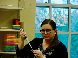 Willoughby in the lab holding a pipette and looking seriously at the camera
